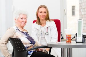 Young female doctor sitting with pensioner in surgery consultation hour at desk