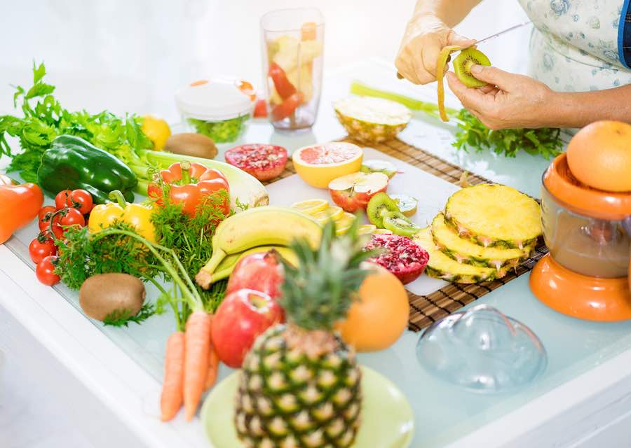 Happy senior couple preparing healthy vegetarian breakfast with fruits and vegetables